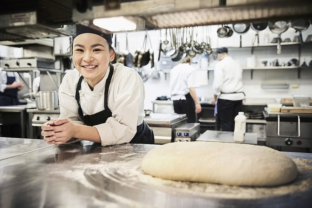Portrait of smiling female chef leaning on counter in commercial kitchen